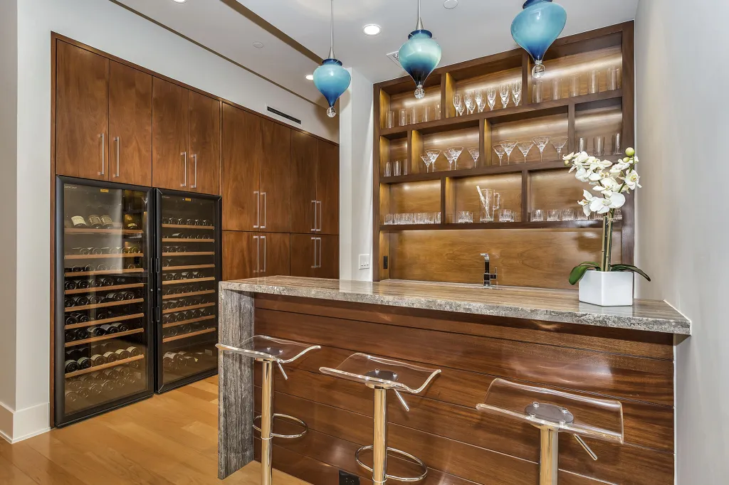 Wet bar with walnut cabinetry, glass-front wine fridges and blue glass pendants
