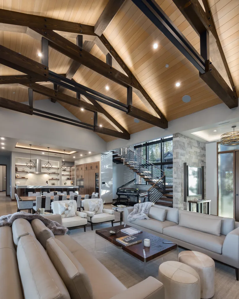 Great room under timber trusses with a long sofa and the kitchen beyond