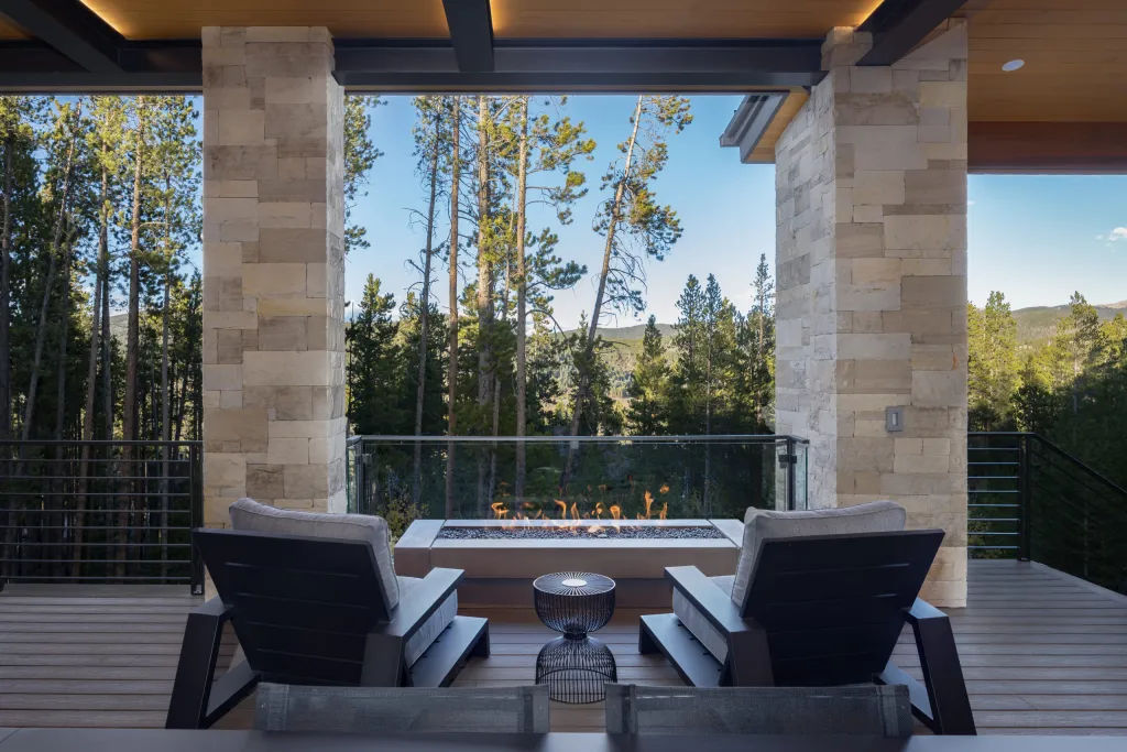 Deck with lounge chairs around a fire table among pine trees