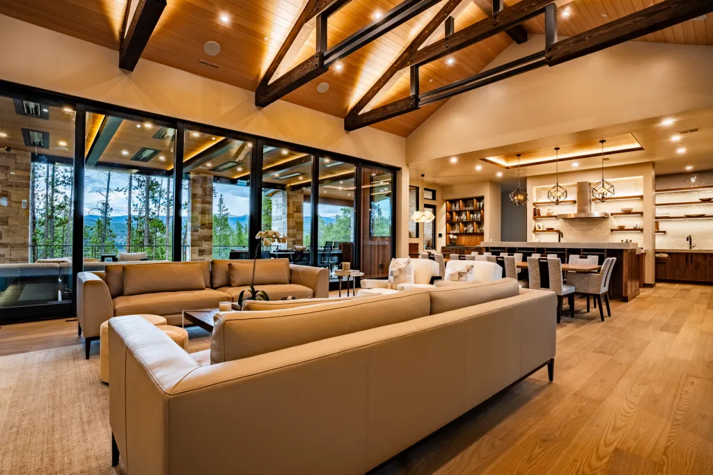 Living room with a long sofa under timber beams and walls of windows