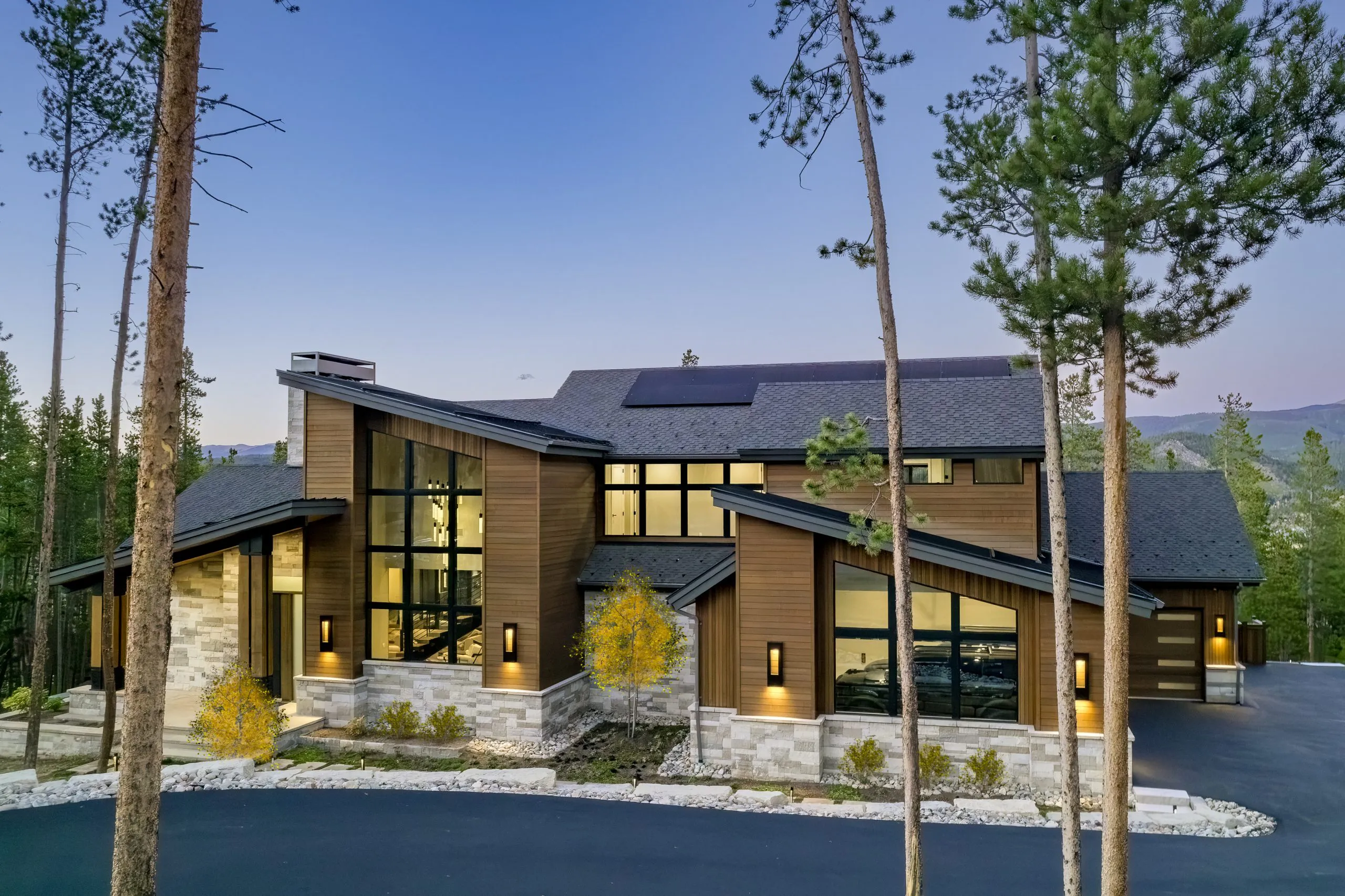 Mountain modern home with timber terraces and stone columns at dusk