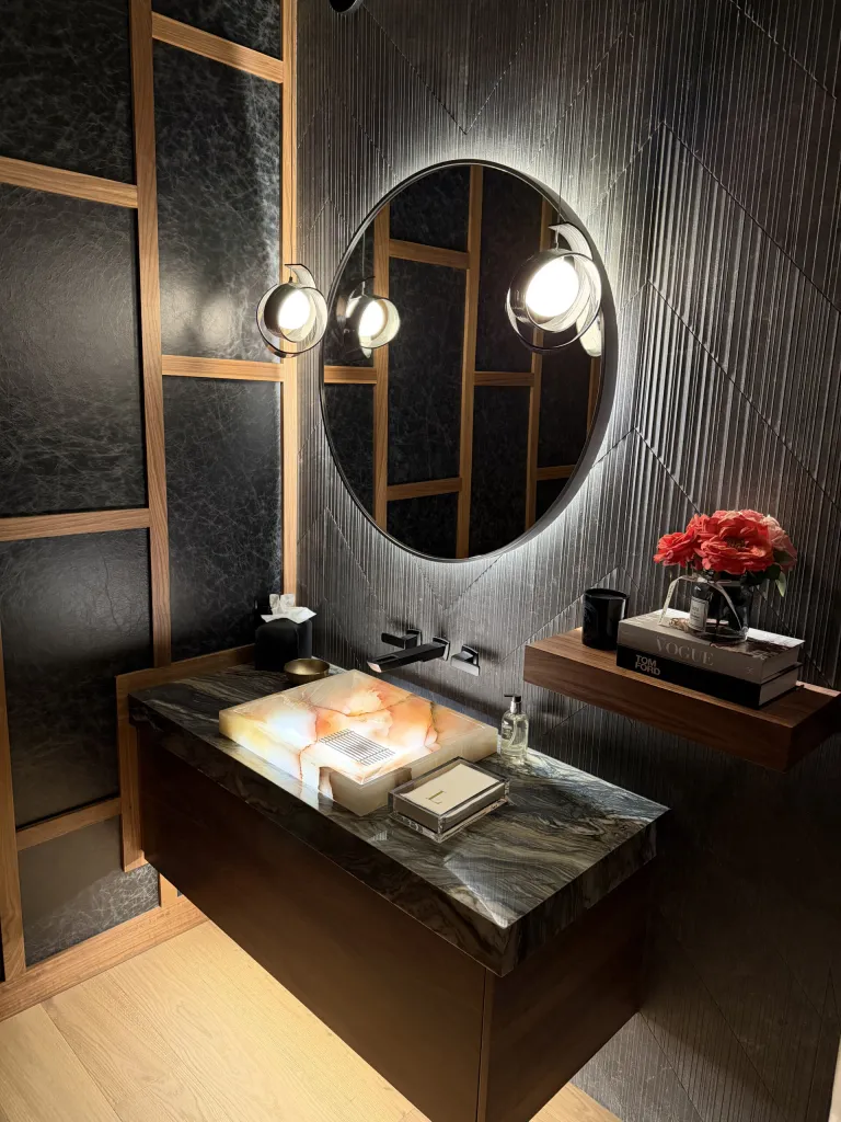 Powder room with a stone vanity and round backlit mirror