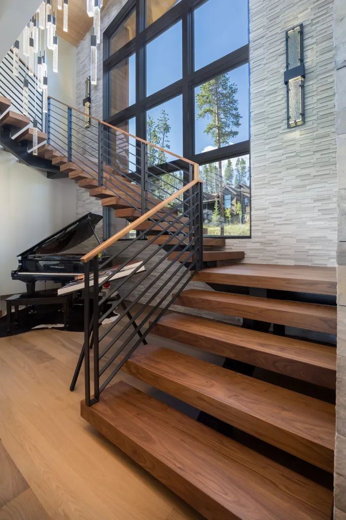 Floating timber staircase with steel railing beside tall windows