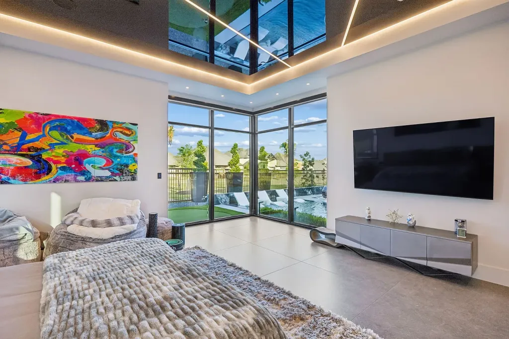 Primary bedroom with a lit tray ceiling, colorful art and pool views