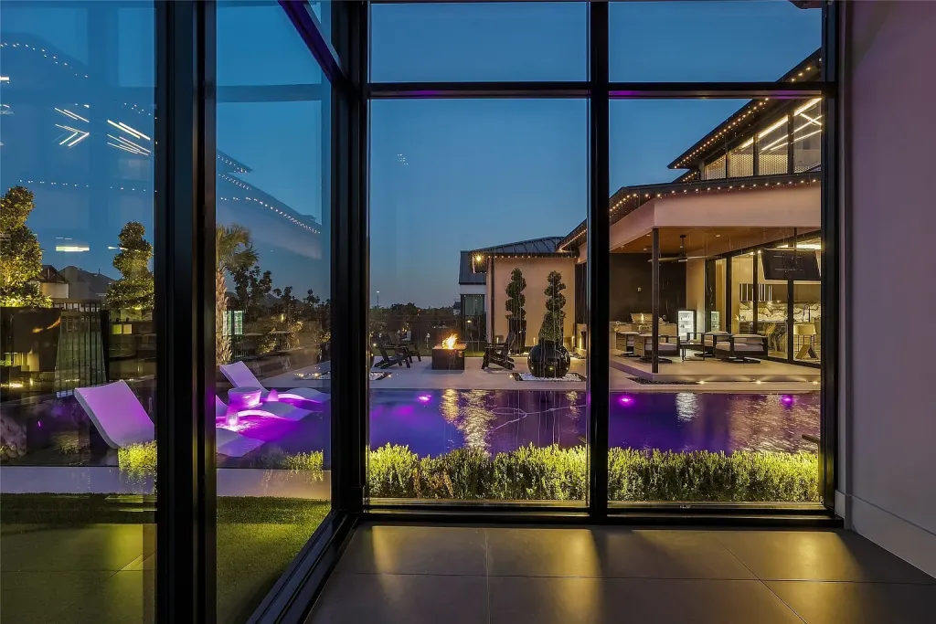 Corner of floor-to-ceiling glass looking out to the lit pool at dusk