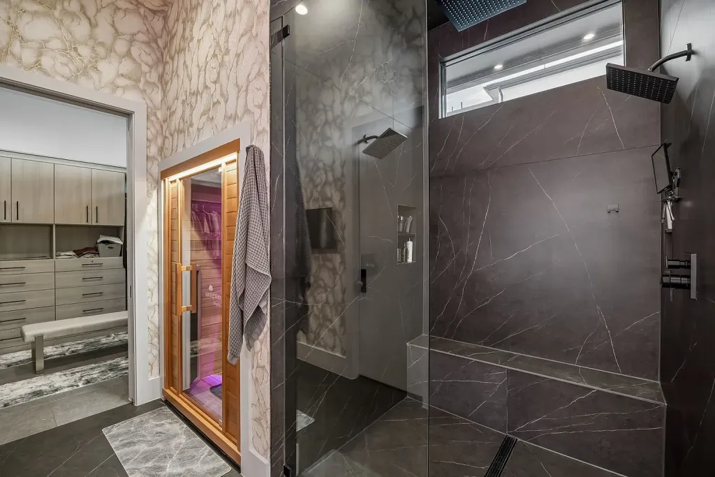 Glass shower with dark stone walls beside a sauna door