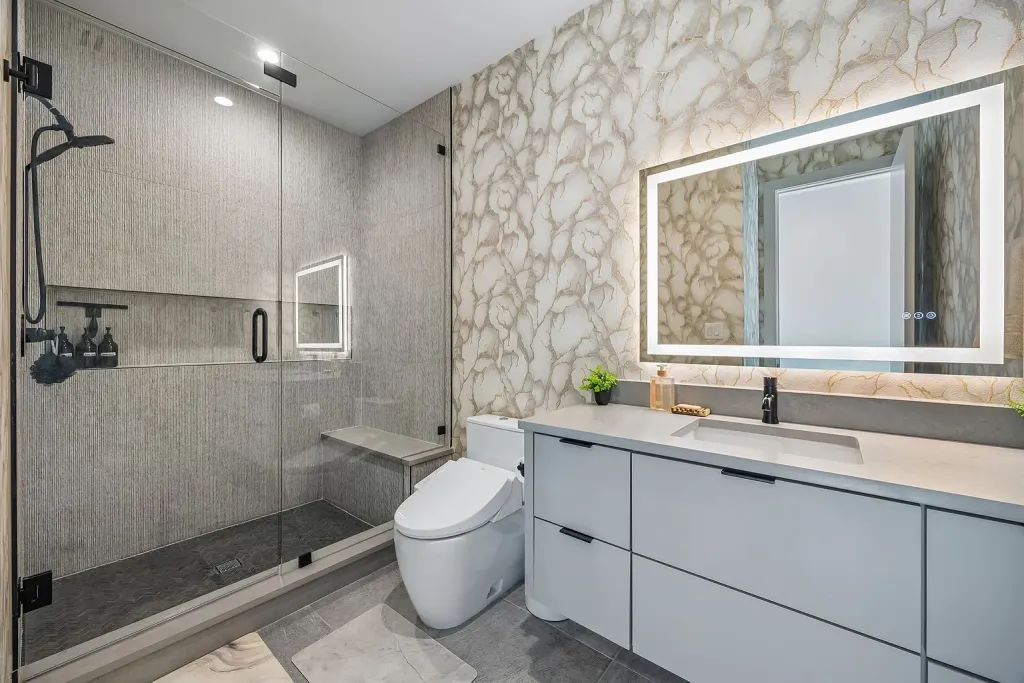 Bathroom with a glass shower, backlit mirror and grey vanity