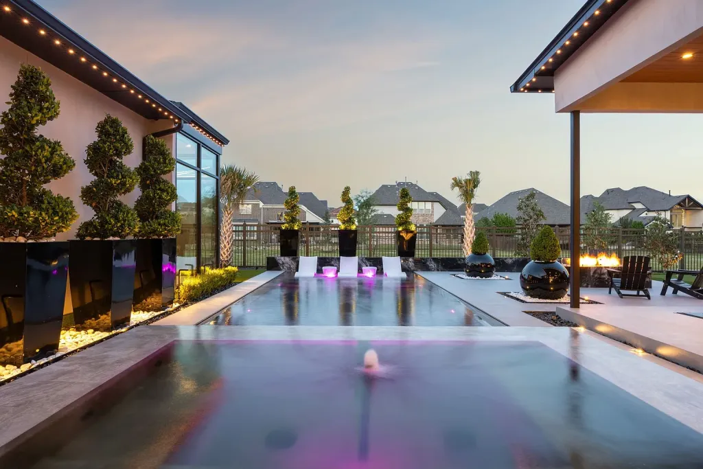 Pool with lit fountains and topiaries at dusk