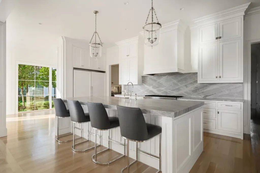 White kitchen with a grey stone island, counter stools and lantern pendants