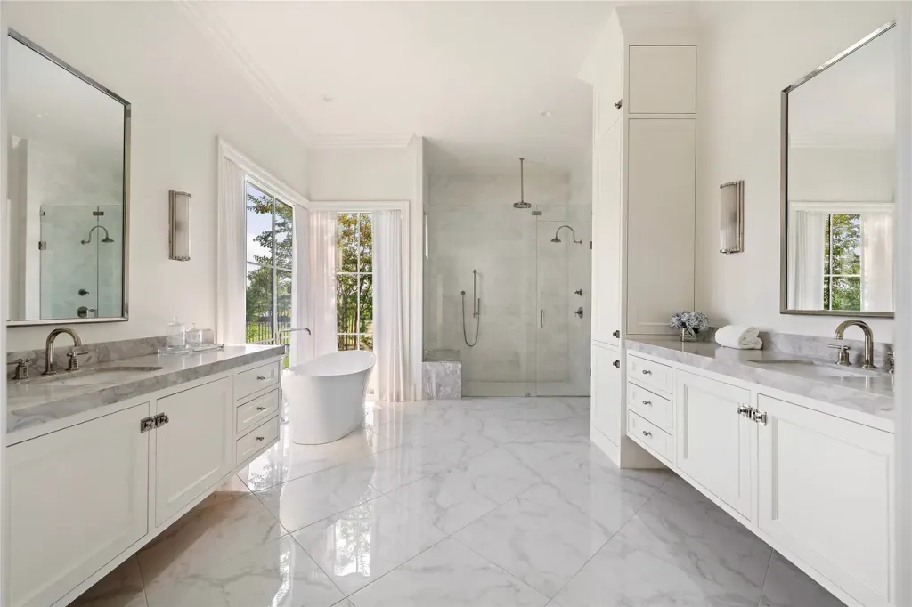 Primary bath with marble floors, a freestanding tub and twin vanities