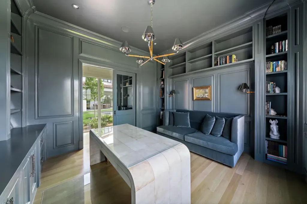 Study with blue-grey panelled walls, built-in shelving and a sputnik chandelier