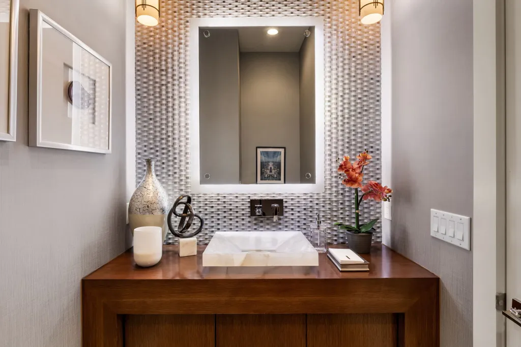 Powder room with a walnut vanity, mosaic tile wall and backlit mirror