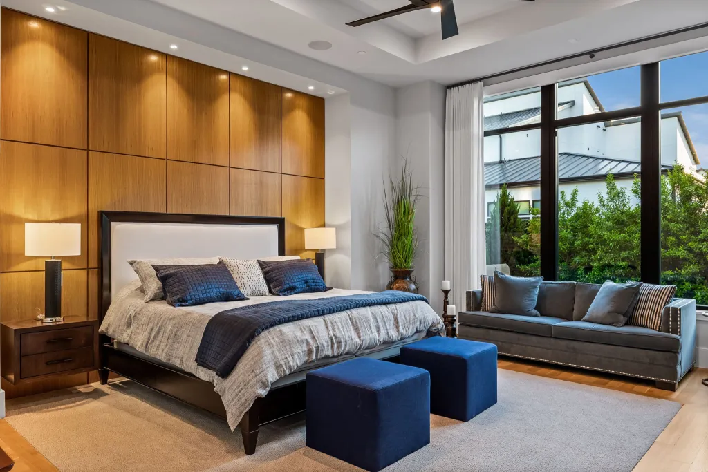 Bedroom with a wood-panelled wall, navy accents and a sitting area by tall windows
