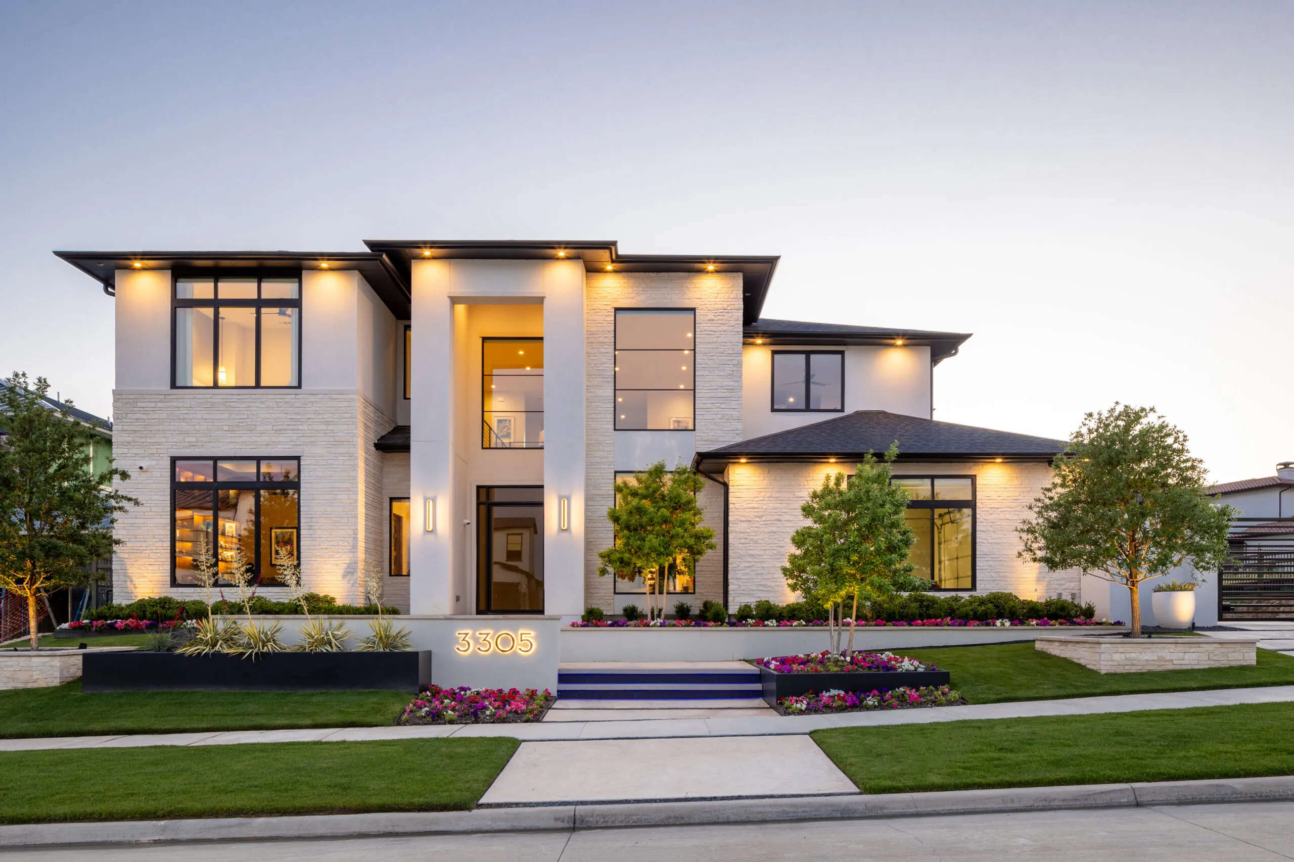 White contemporary home with dark trim lit at dusk